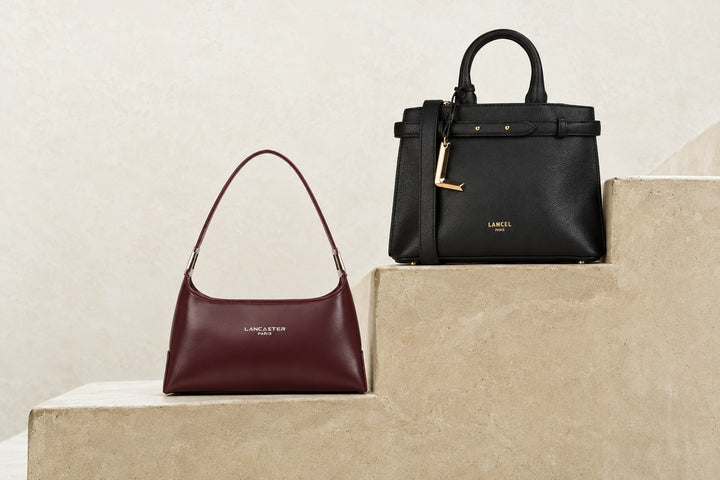 Sac Lancaster Suave Ace bordeaux et sac Lancel Faubourg noir posés sur un escalier en pierre claire