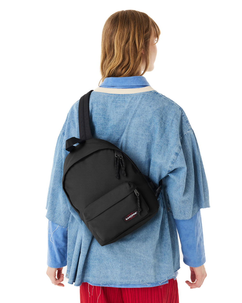 Eastpak Orbit black backpack worn on the back with a blue jacket and red trousers.