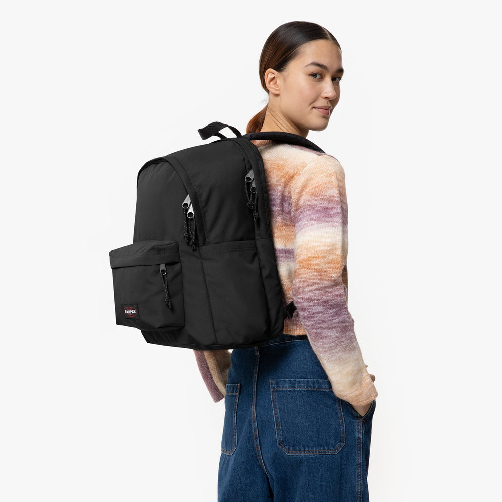 Eastpak Rucksak Day Office a schwaarz um Réck, mat engem gesträifte Pullover a bloe Jeans.