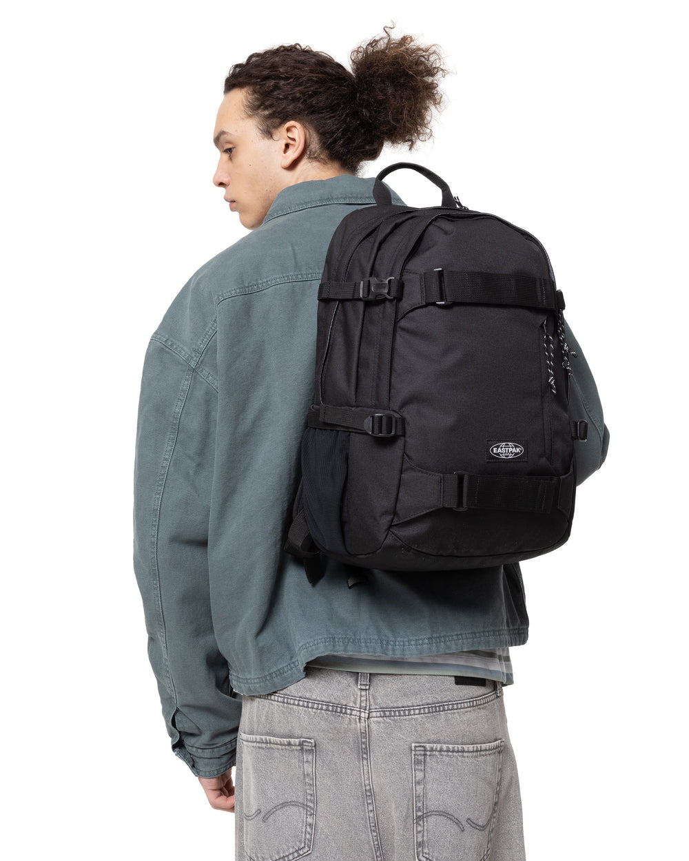 Eastpak rucsac negru GETTER PRO purtat pe spate, cu o jachetă gri-albăstruie și blugi gri.