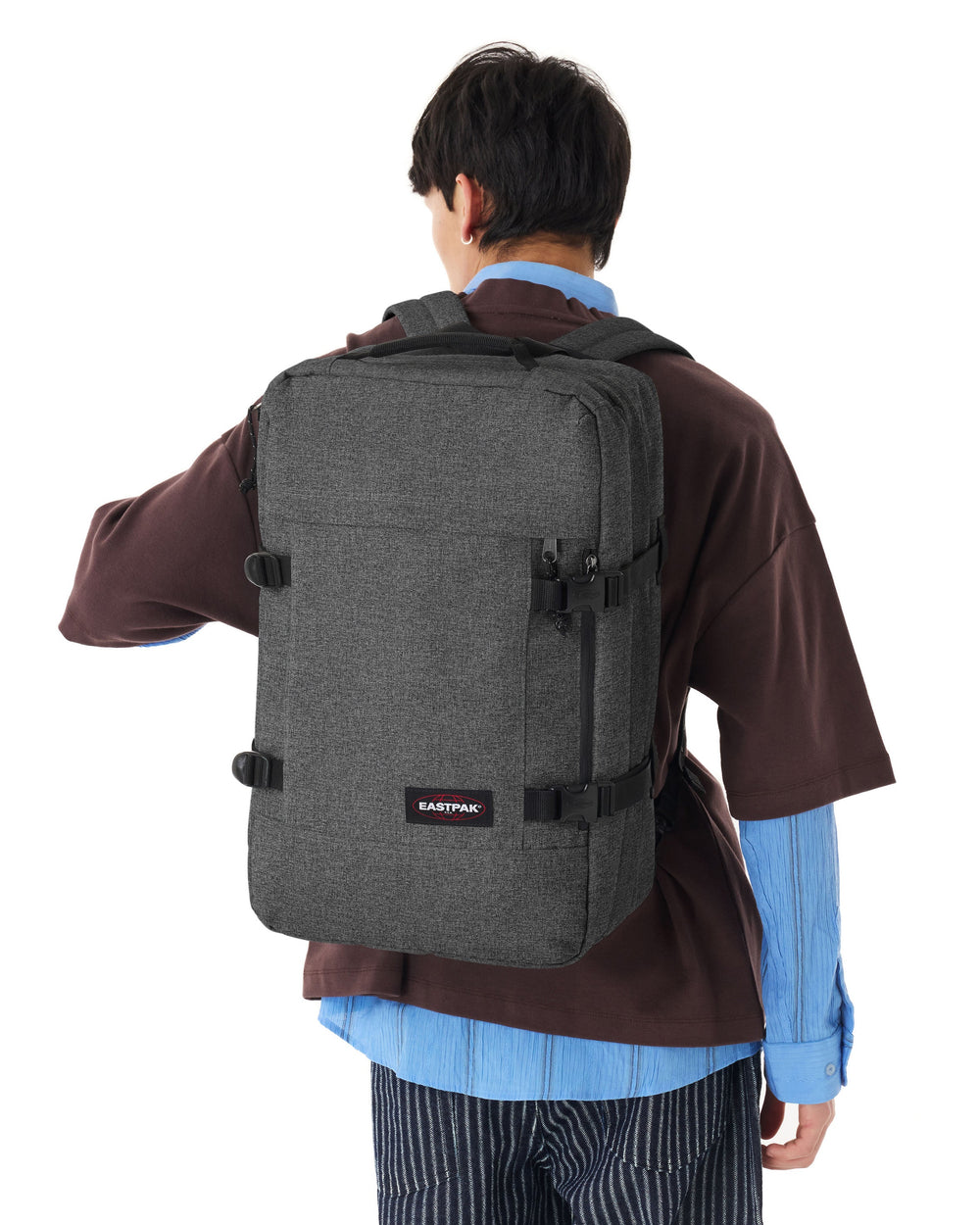 Eastpak Rucksack Travelpack grau auf dem Rücken getragen, zu einem blauen Hemd und einem braunen Oberteil.