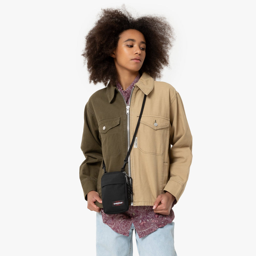 Eastpak TH shoulder bag in black, worn crossbody with a two-tone jacket and a pink shirt.