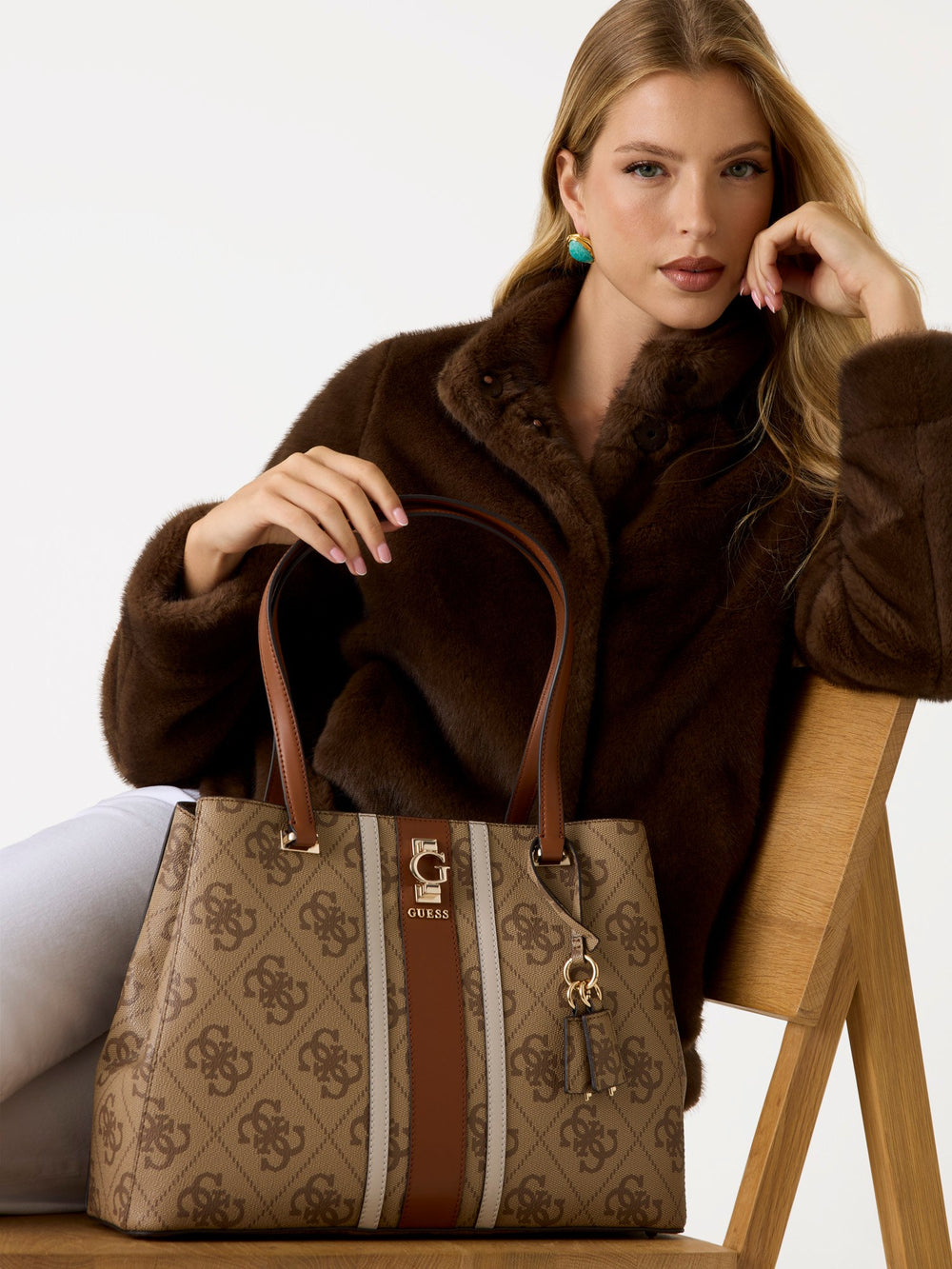 Guess bruine Handbag-shopper in de hand, met een bruine jas en een witte broek.