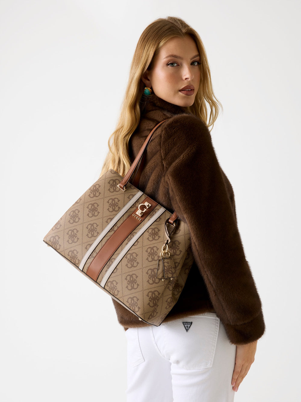 Guess bruine Handbag-shopper over de schouder, bij een bruin jasje en een witte broek.