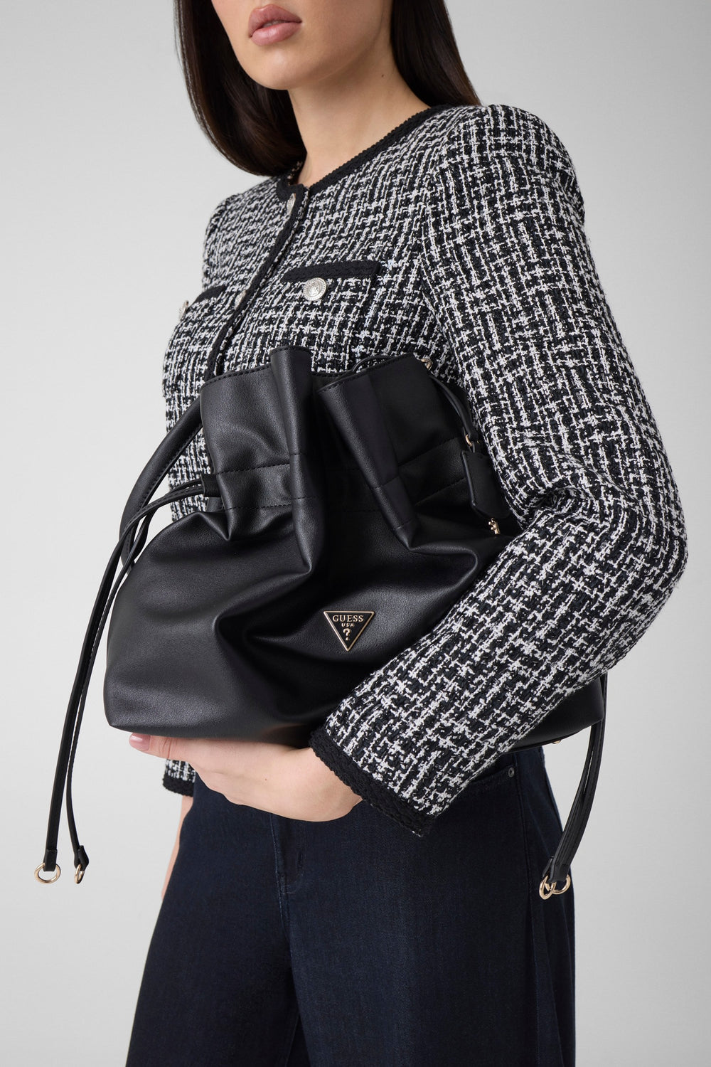 Guess schwaarze Karima-Shopper an der Hand, mat enger schwaarz-wäisser Jackett an enger donkeler Box.