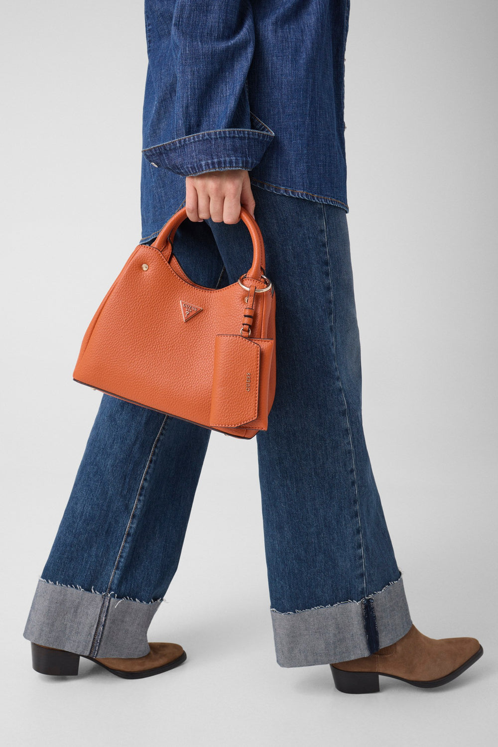 Guess Shopper Lorella Petit a Braun, an der Hand gehalen zu enger bloer Jeans mat ëmgeschloene Saumen a bronge Schong.