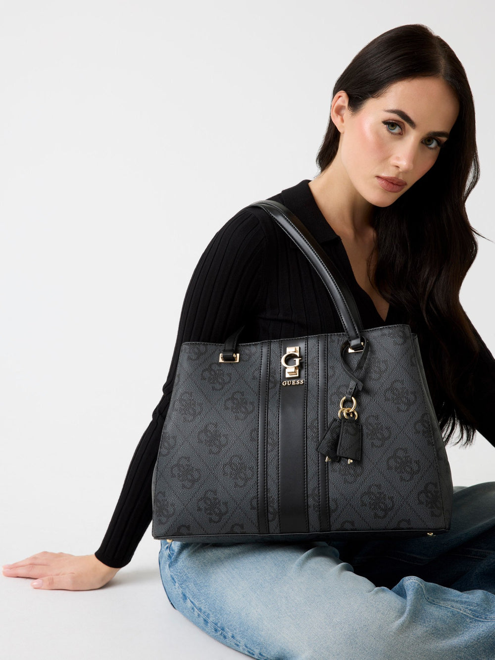 Guess zwarte Handbag-shopper, over de schouder gedragen bij een zwarte top en lichtblauwe jeans.