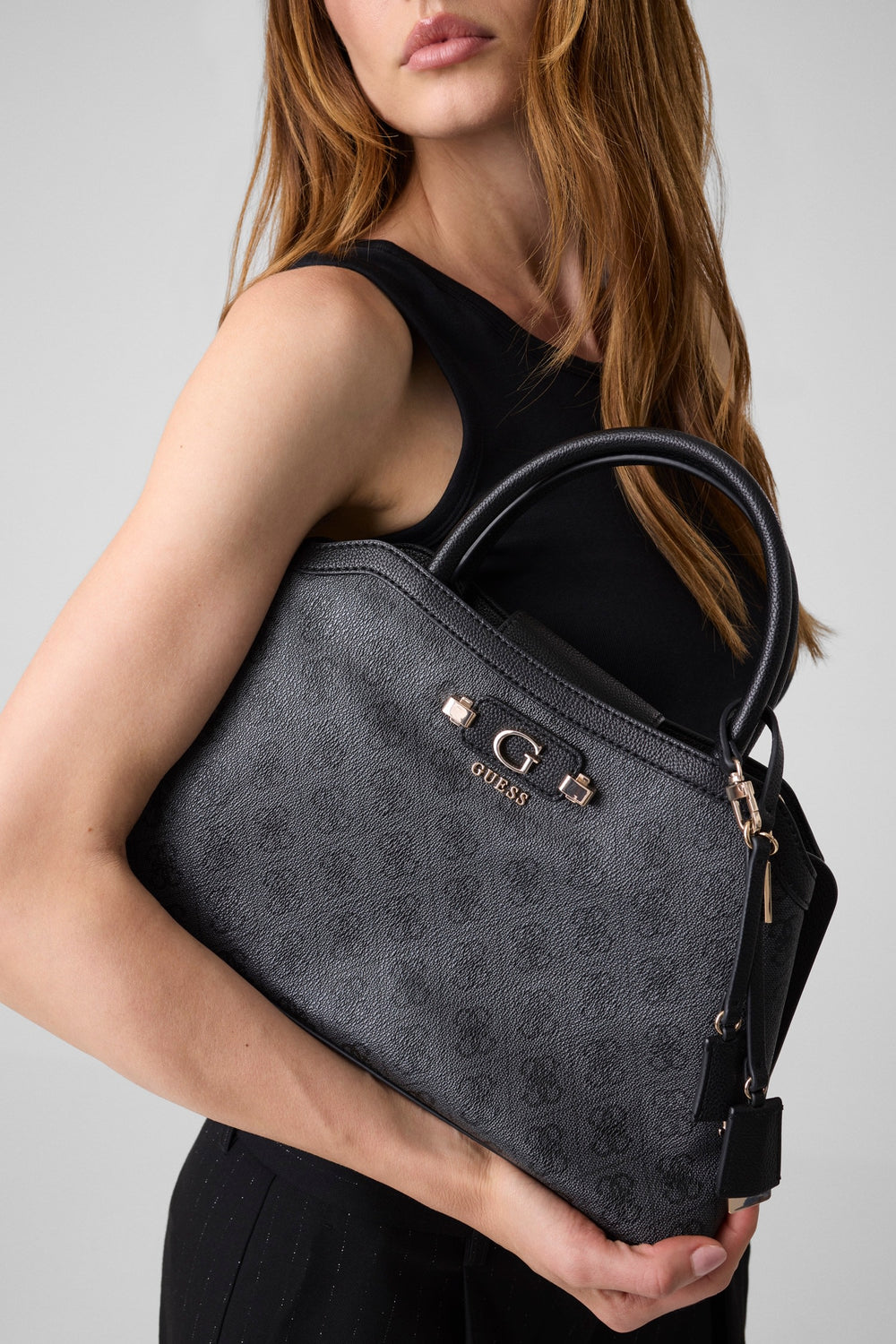 Guess zwarte handtas Lindsey, in de hand gedragen, met een zwarte top en zwarte broek.