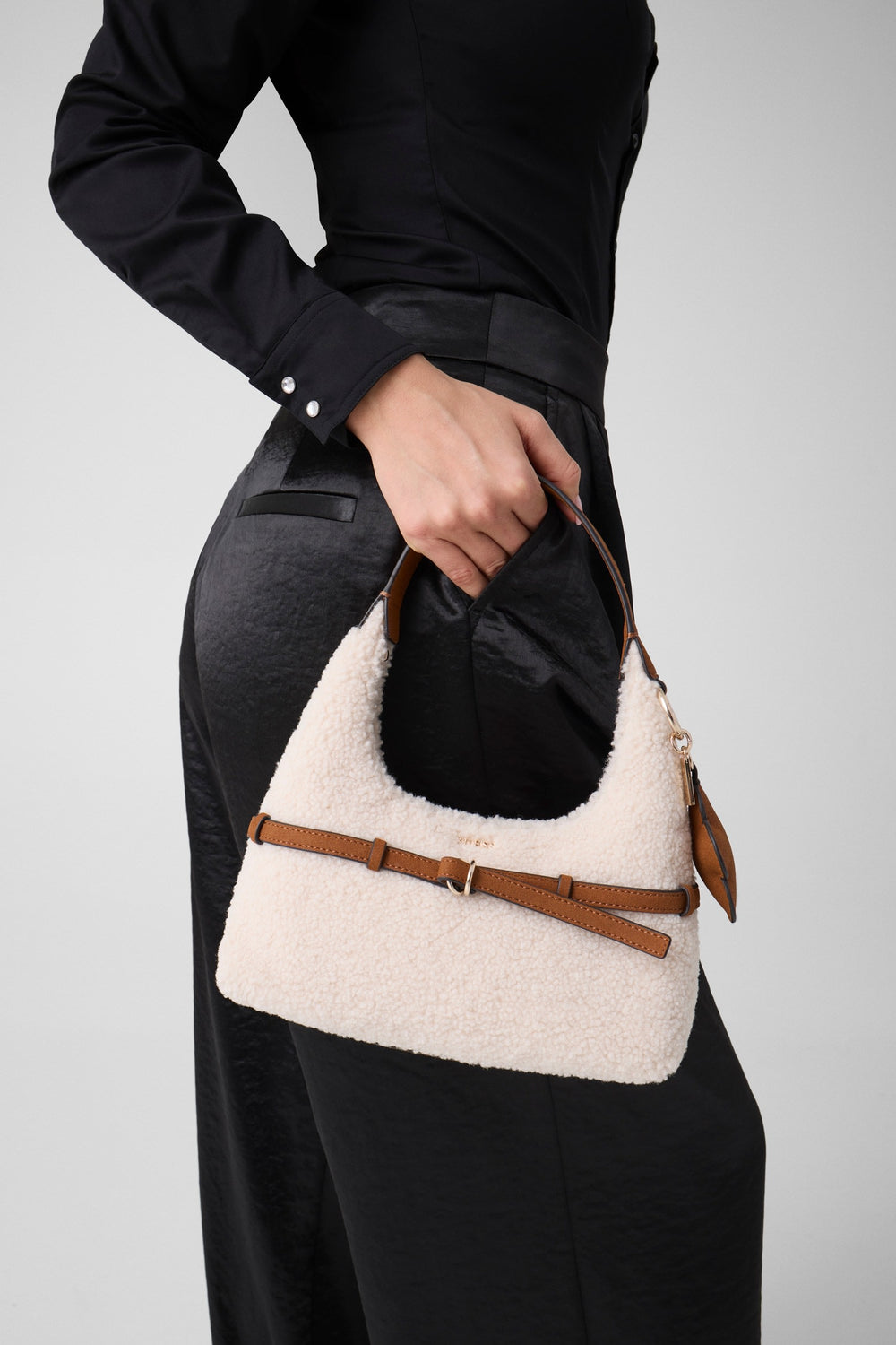 Guess sac Hobo Taylor Mini blanc tenu à la main avec une tenue noire.