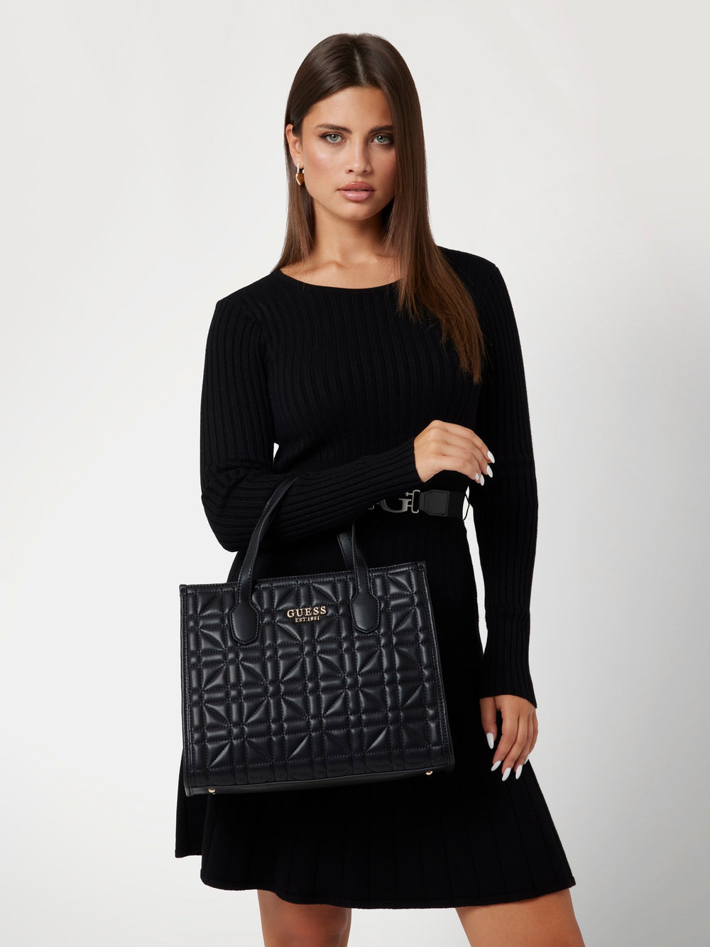 Guess flap bag Adam Convertible Xbo in black, held by hand in front of a black outfit.