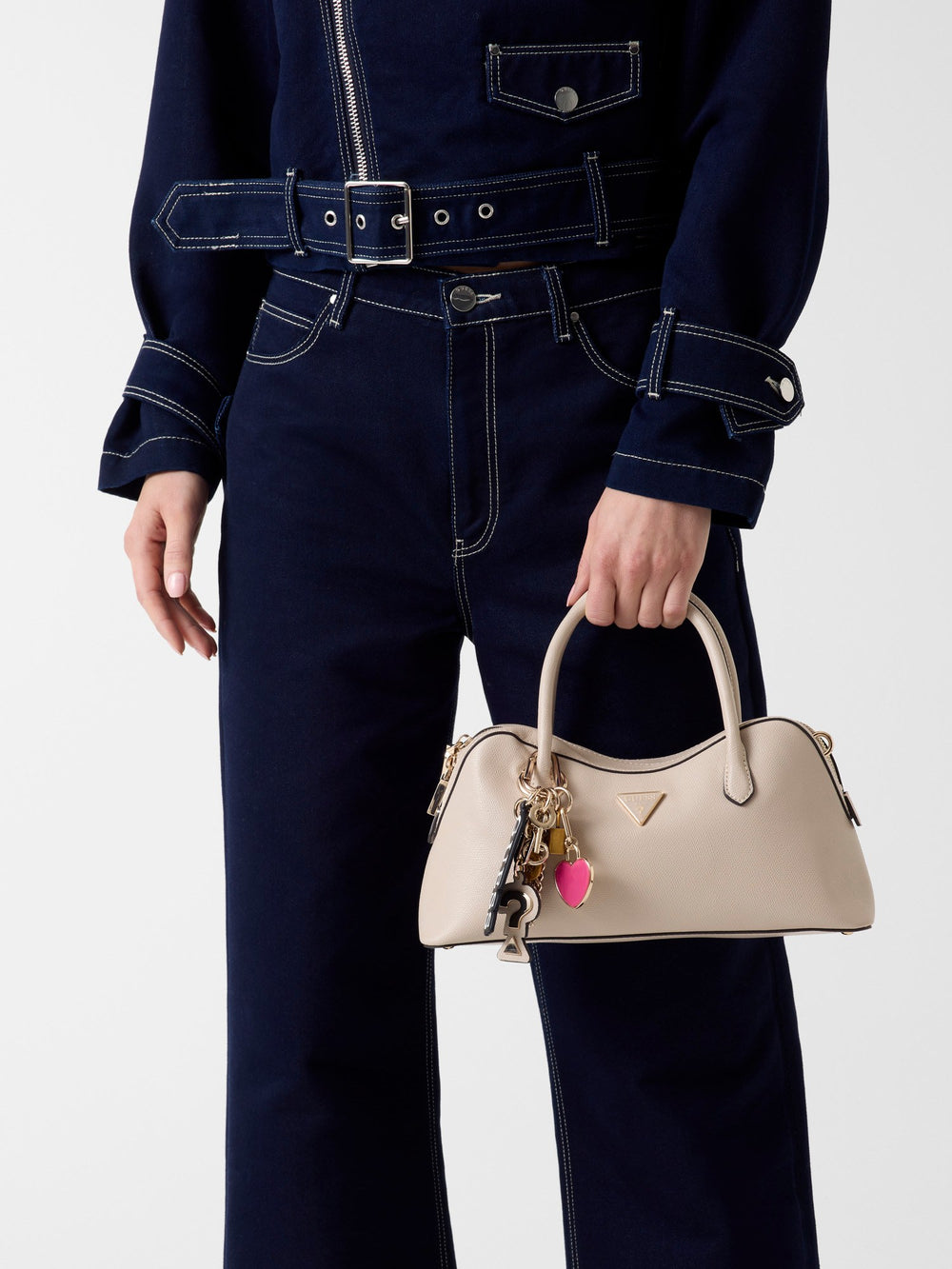 Guess sac à main Davina marron tenu à la main, avec une veste et un jean bleu marine.