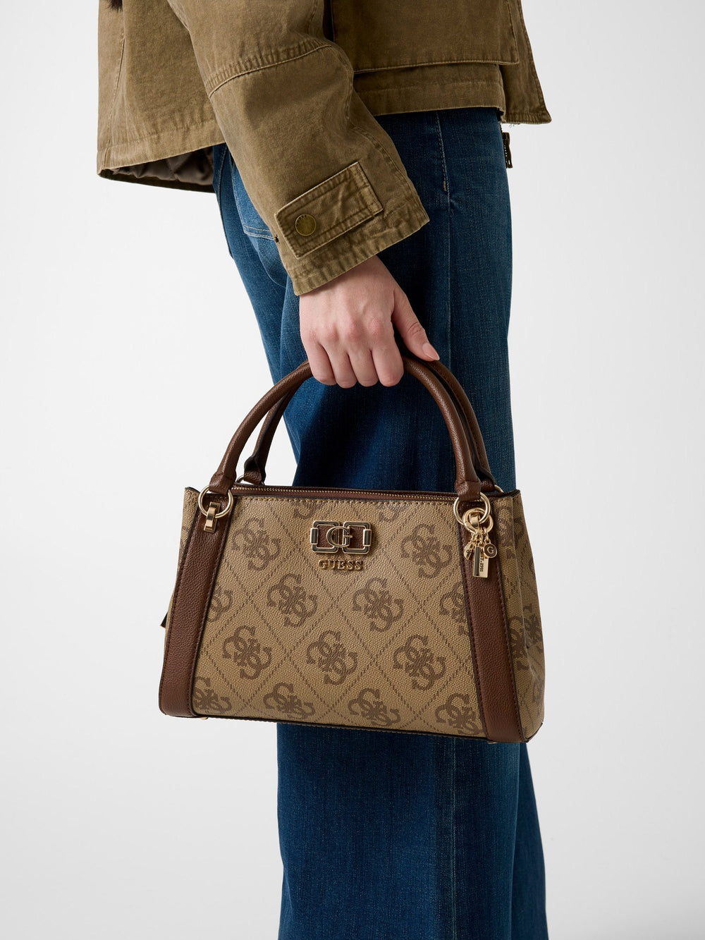 Guess borsa a secchiello Karnilla Logo Bucket marrone, tenuta a mano con una giacca color kaki e jeans blu.