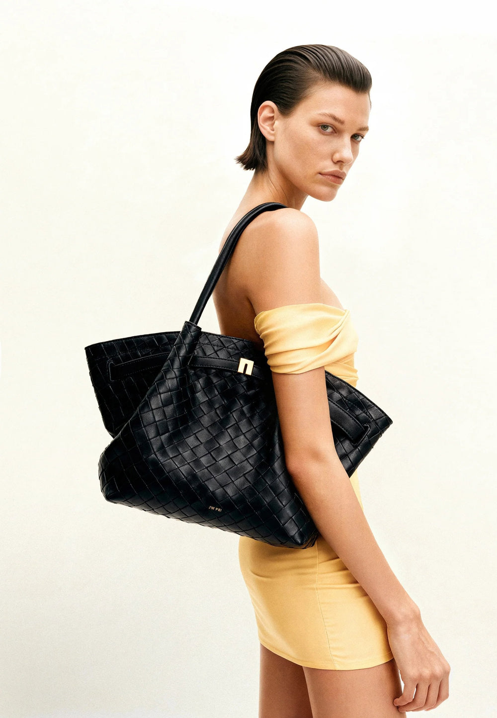 Cabas JW PEI Hana noir porté à l'épaule par une femme en robe jaune, vue de profil