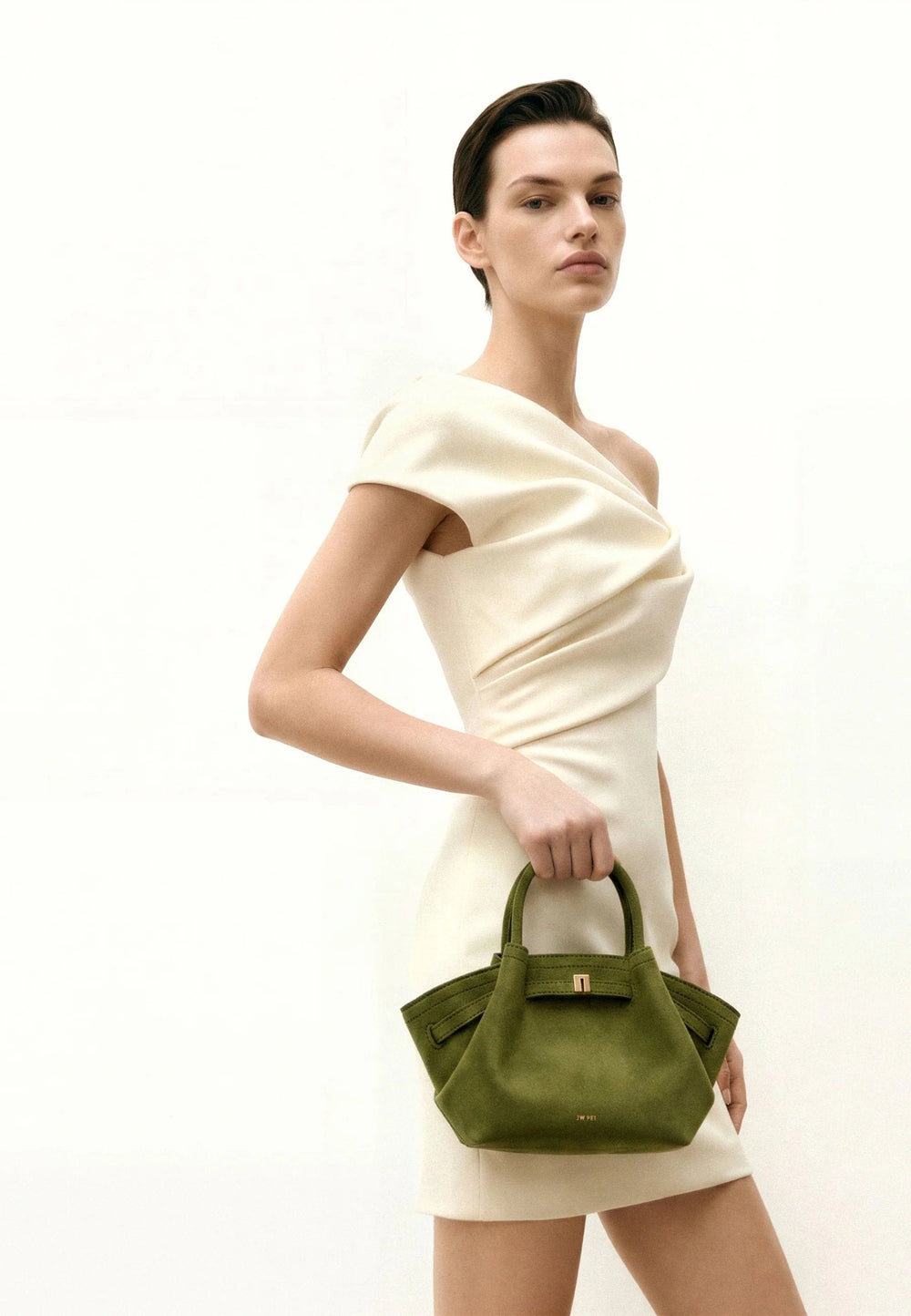 Cabas JW PEI Hana vert olive foncé, porté à la main, avec une robe crème asymétrique.