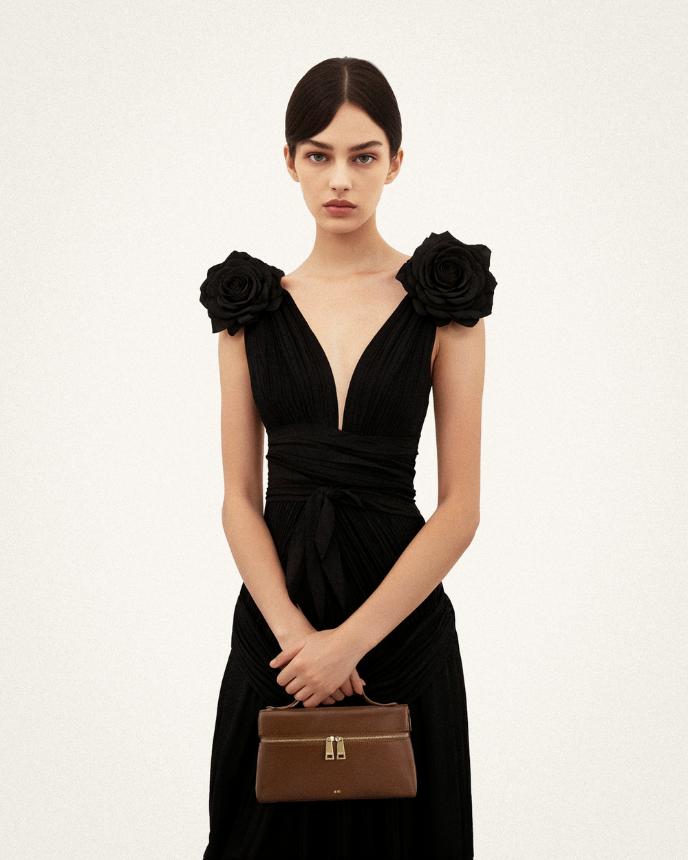 JW PEI bolso de mano Thea marrón sostenido en la mano delante de un vestido negro.