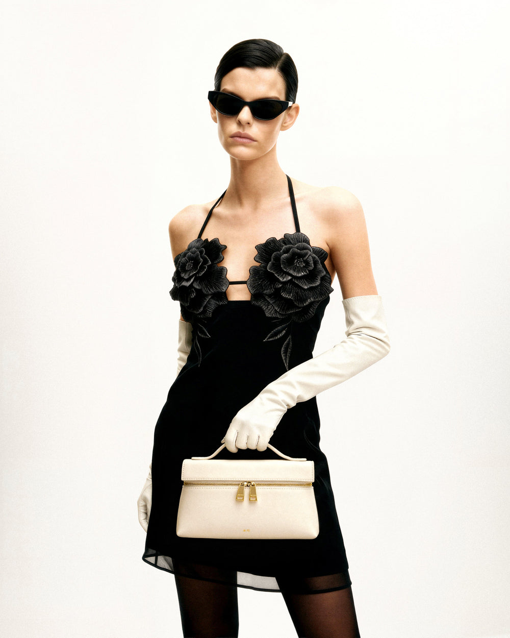 JW PEI bolso de mano Thea blanco sostenido en la mano, con un vestido negro y guantes blancos.