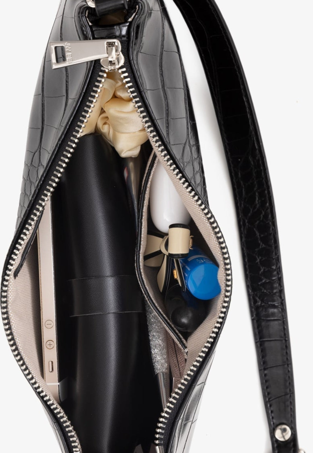 Intérieur du sac bandoulière JW PEI Eva Black Croc, montrant un téléphone, des écouteurs, un rouge à lèvres et d'autres accessoires.