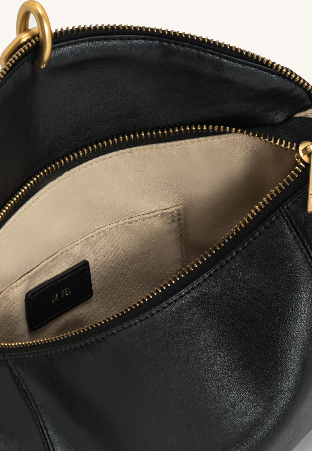 Intérieur d'un sac bandoulière JW PEI Jayla noir, avec une étiquette logo dorée sur fond beige