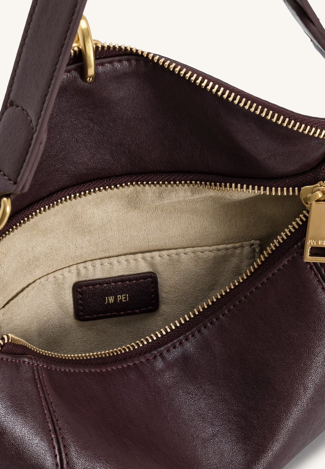 Intérieur d'un sac bandoulière JW PEI Jayla Deep Red en simili cuir avec une poche intérieure et le logo de la marque.