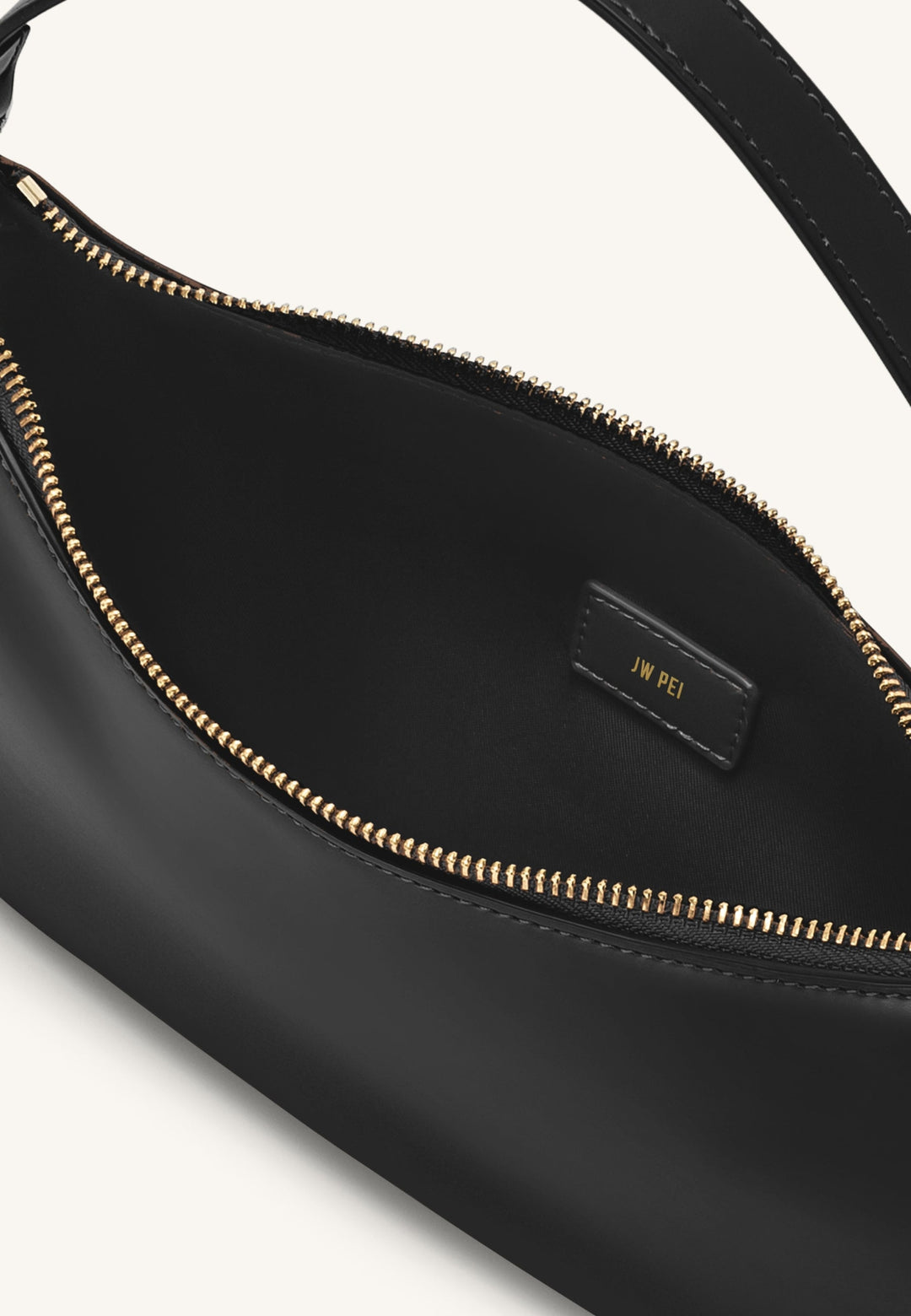 Intérieur du sac bandoulière JW PEI Lily noir avec logo doré "JW PEI" sur une étiquette en cuir