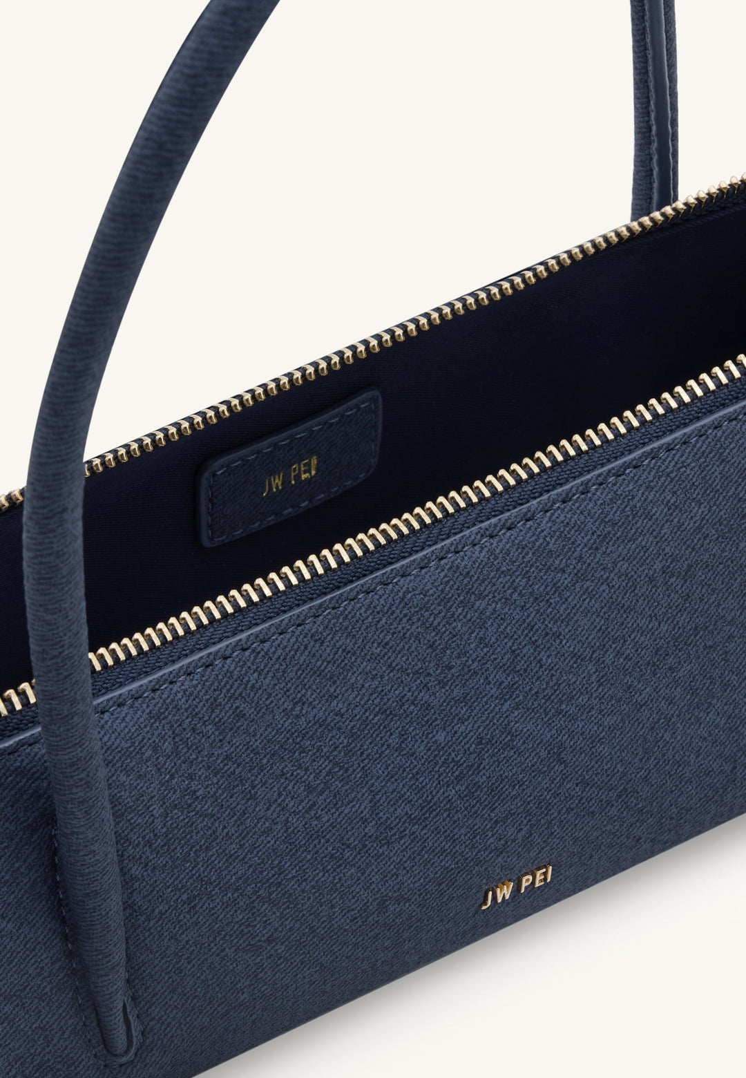 Intérieur d'un sac bandoulière JW PEI Nova bleu denim, montrant la fermeture éclair dorée et le logo de la marque