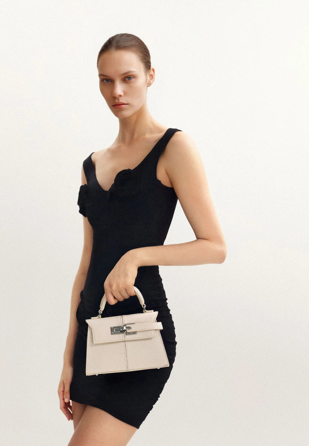 Sac à main JW PEI Elise blanc porté à la main, devant un fond blanc