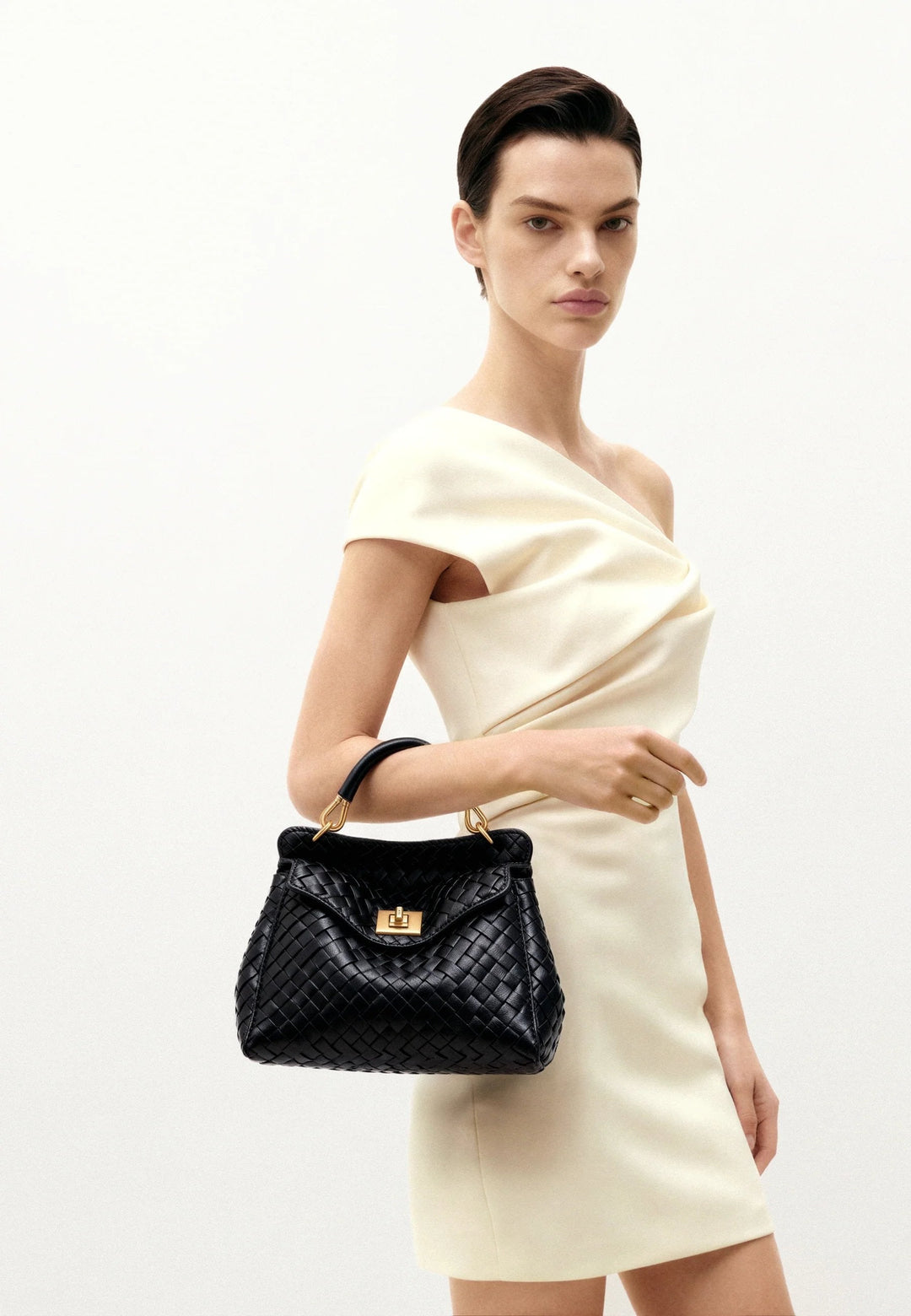 Sac à main JW PEI Lucia noir en simili cuir tressé, porté à la main, avec fermeture magnétique dorée.
