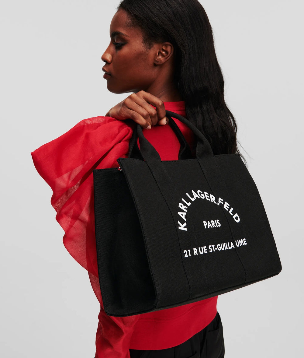Karl Lagerfeld svart Essentials-shopper buren i handen, med en röd blus och svarta byxor.