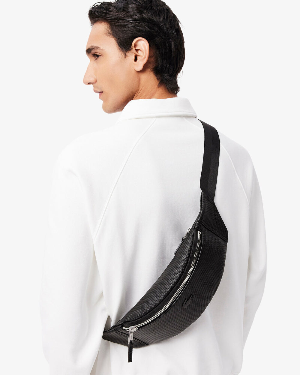 Lacoste banane Chantaco noire portée en bandoulière dans le dos avec une chemise blanche.
