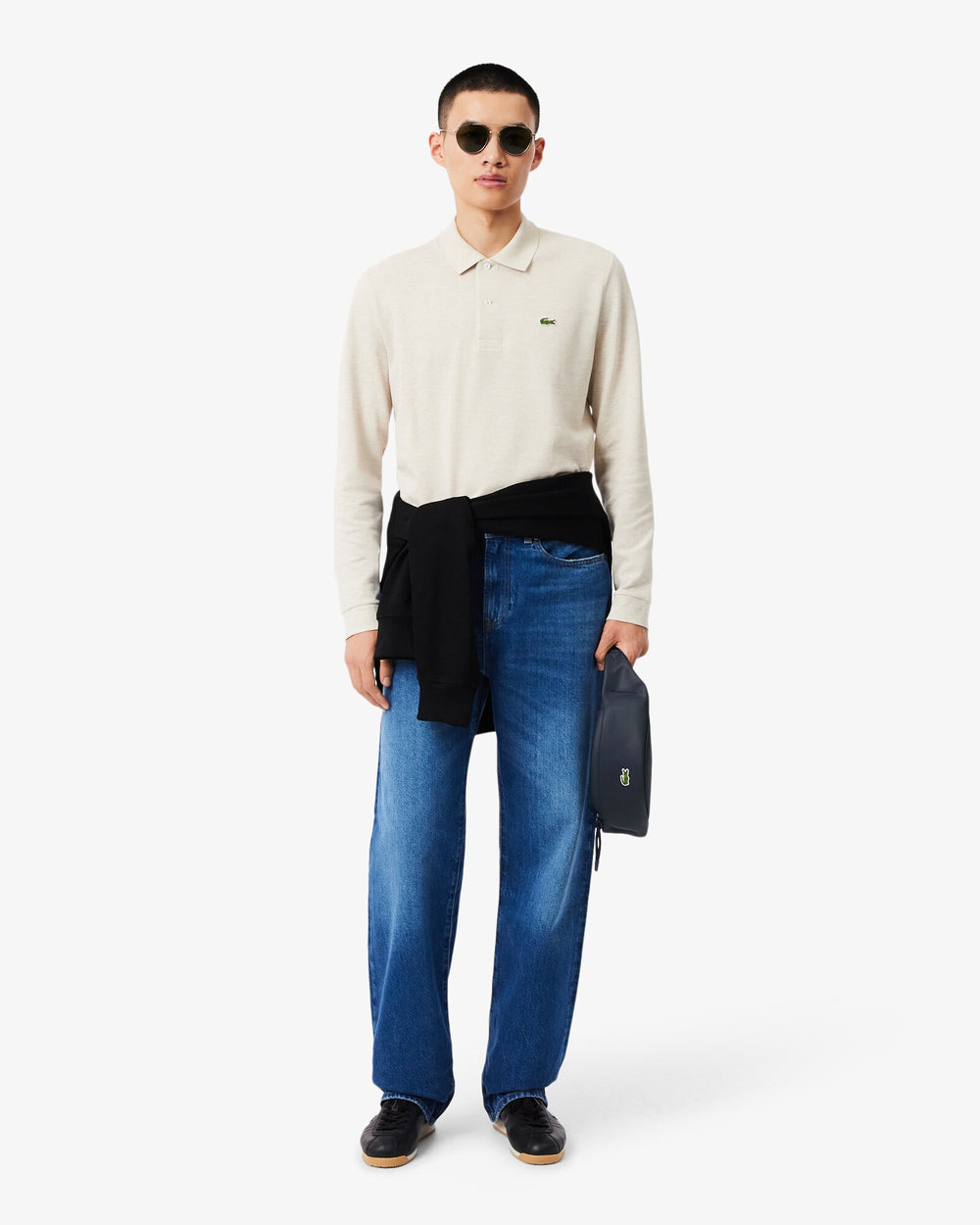 Lacoste Gürteltasche Lcst in Blau, in der Hand gehalten, zu cremeweißem Polohemd und blauen Jeans.
