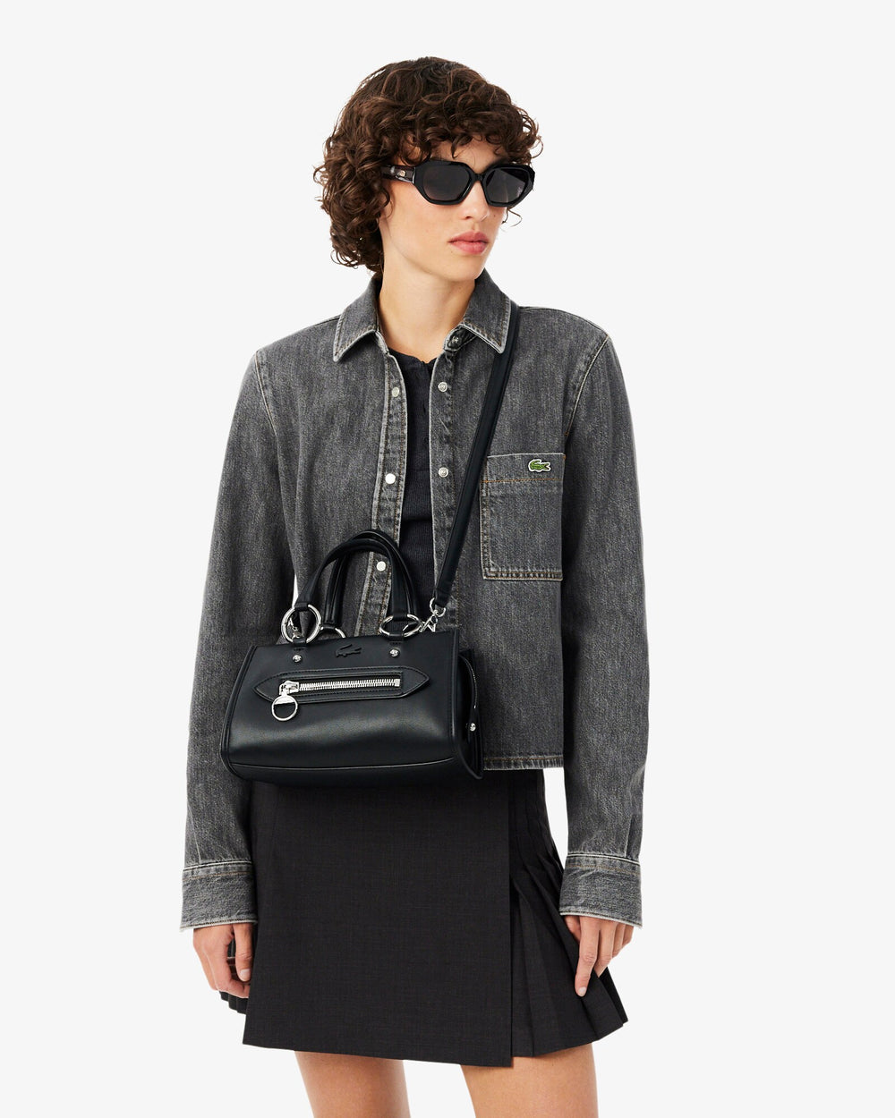 Lacoste shopper Celys preto ao ombro, com casaco cinzento e saia preta.