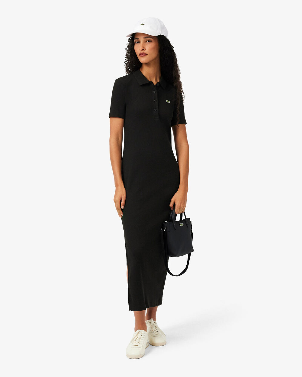 Lacoste cabas L.12.12 Concept noir tenu à la main, avec une robe noire et des baskets blanches.