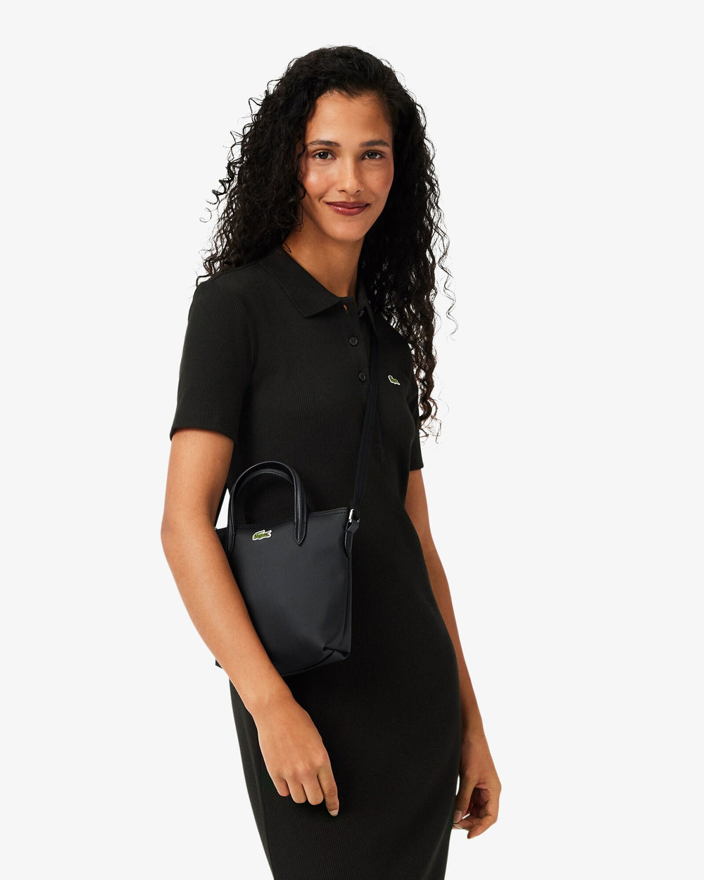 Lacoste cabas L.12.12 Concept noir porté en bandoulière avec une robe noire à manches courtes.