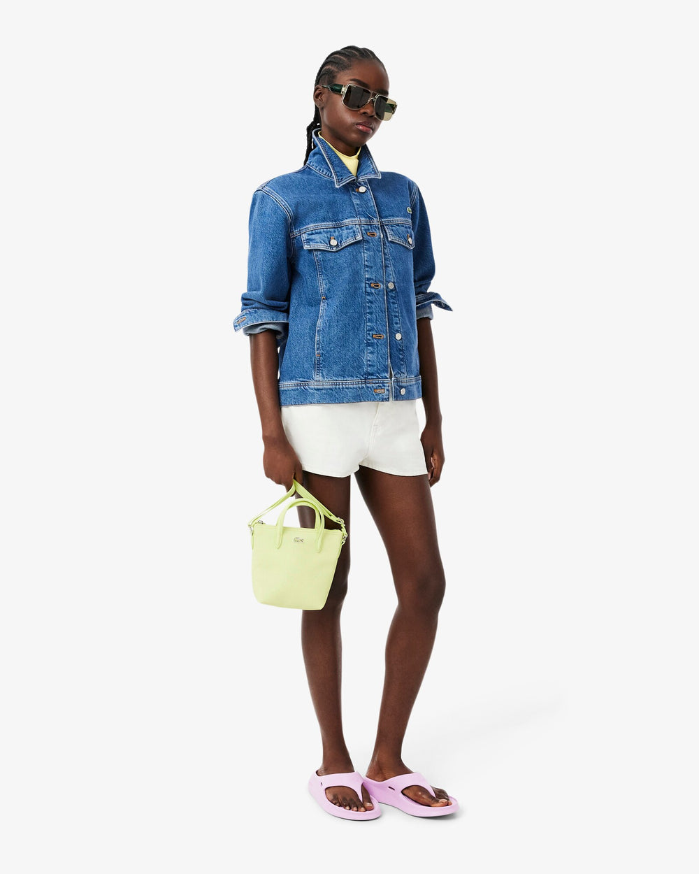 Lacoste cabas L.12.12 Concept vert tenu à la main, avec une veste en jean bleue et un short blanc.