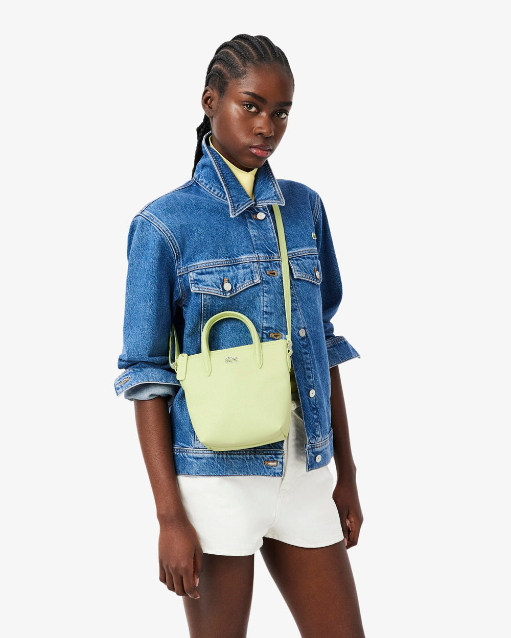 Lacoste cabas L.12.12 Concept vert porté en bandoulière avec une veste en jean bleue et un short blanc.
