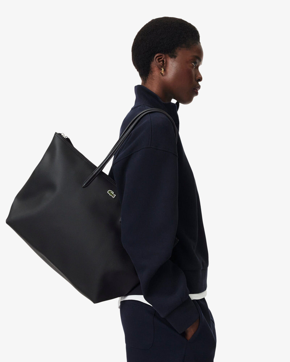 Lacoste čierna nákupná taška L.12.12 Concept, nosená na pleci k tmavomodrému kompletu.
