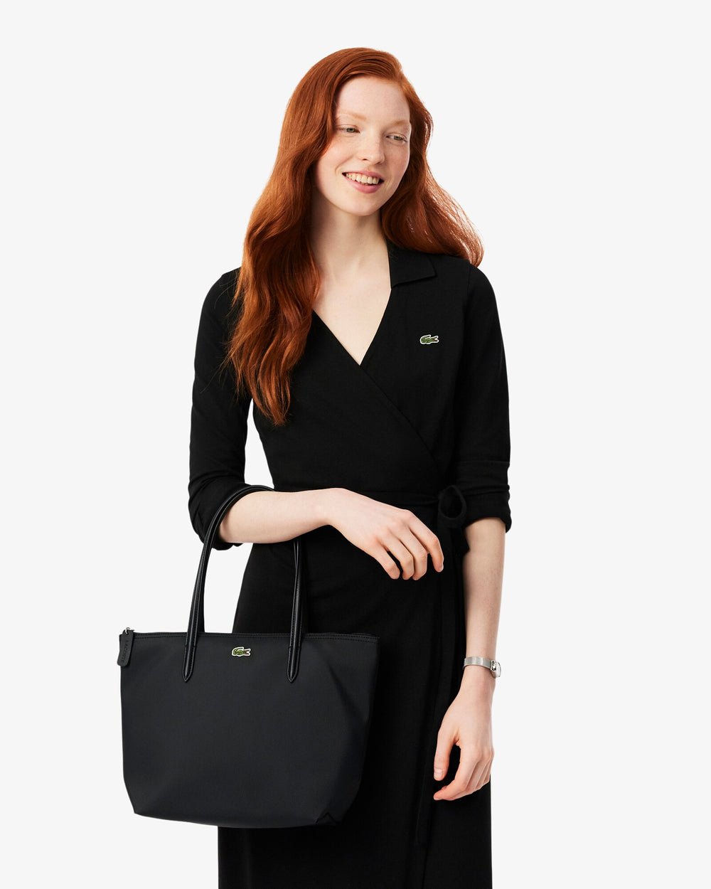 Lacoste saco de compras L.12.12 Concept preto, levado na mão diante de um vestido preto.