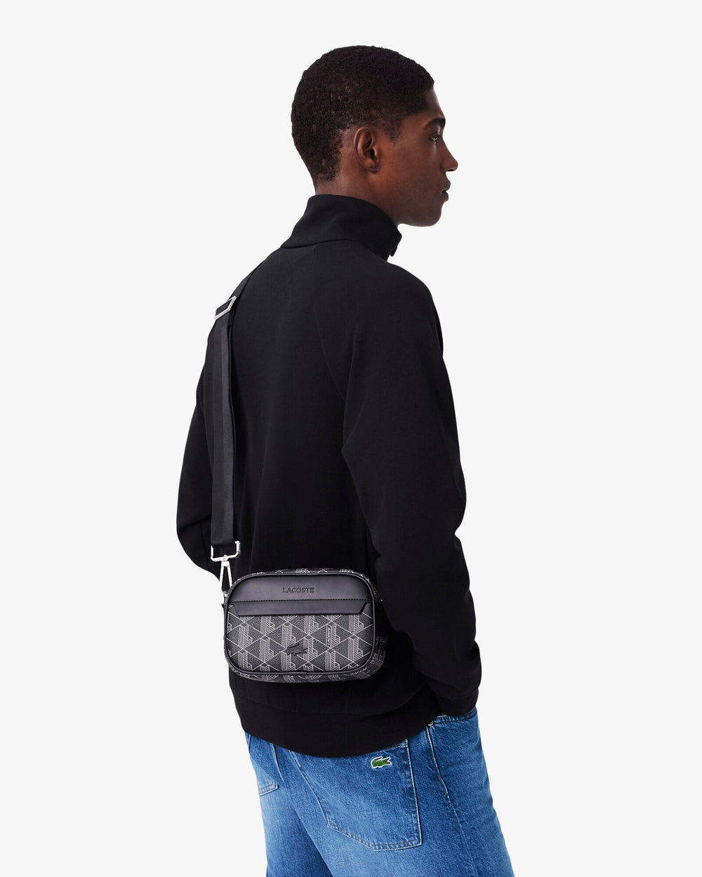 Lacoste must The Blend Camera-kott kantuna üle keha koos musta ülaosa ja siniste teksadega.