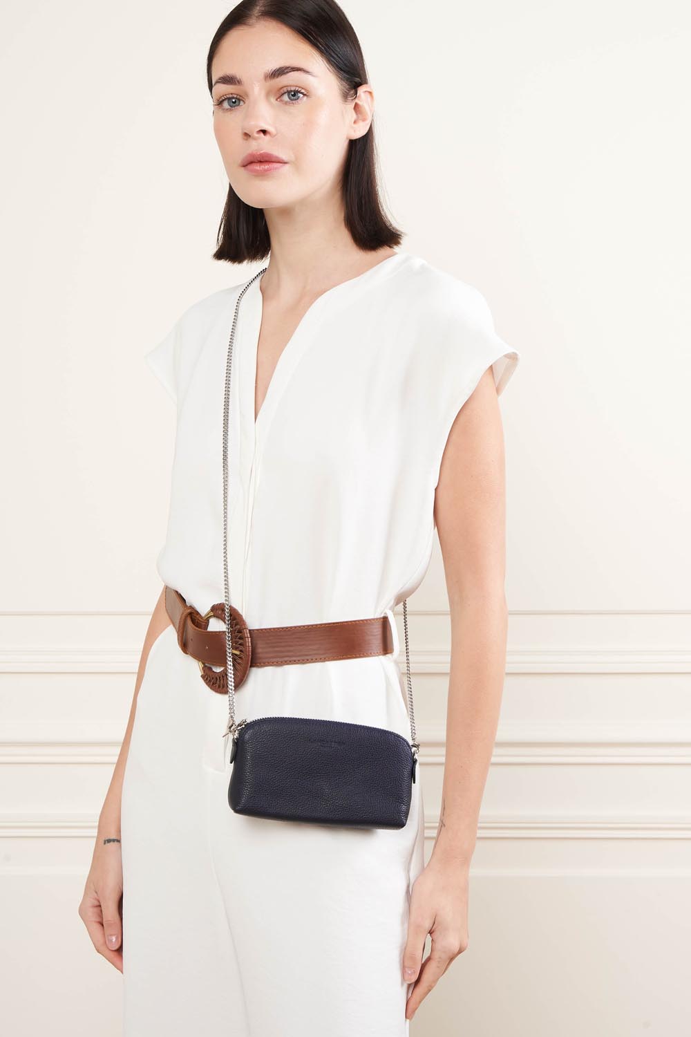 Lancaster Porte monnaie cuir Paris PM Noir – En bleu, le porte-monnaie se porte en bandoulière sur une robe blanche et une ceinture marron.