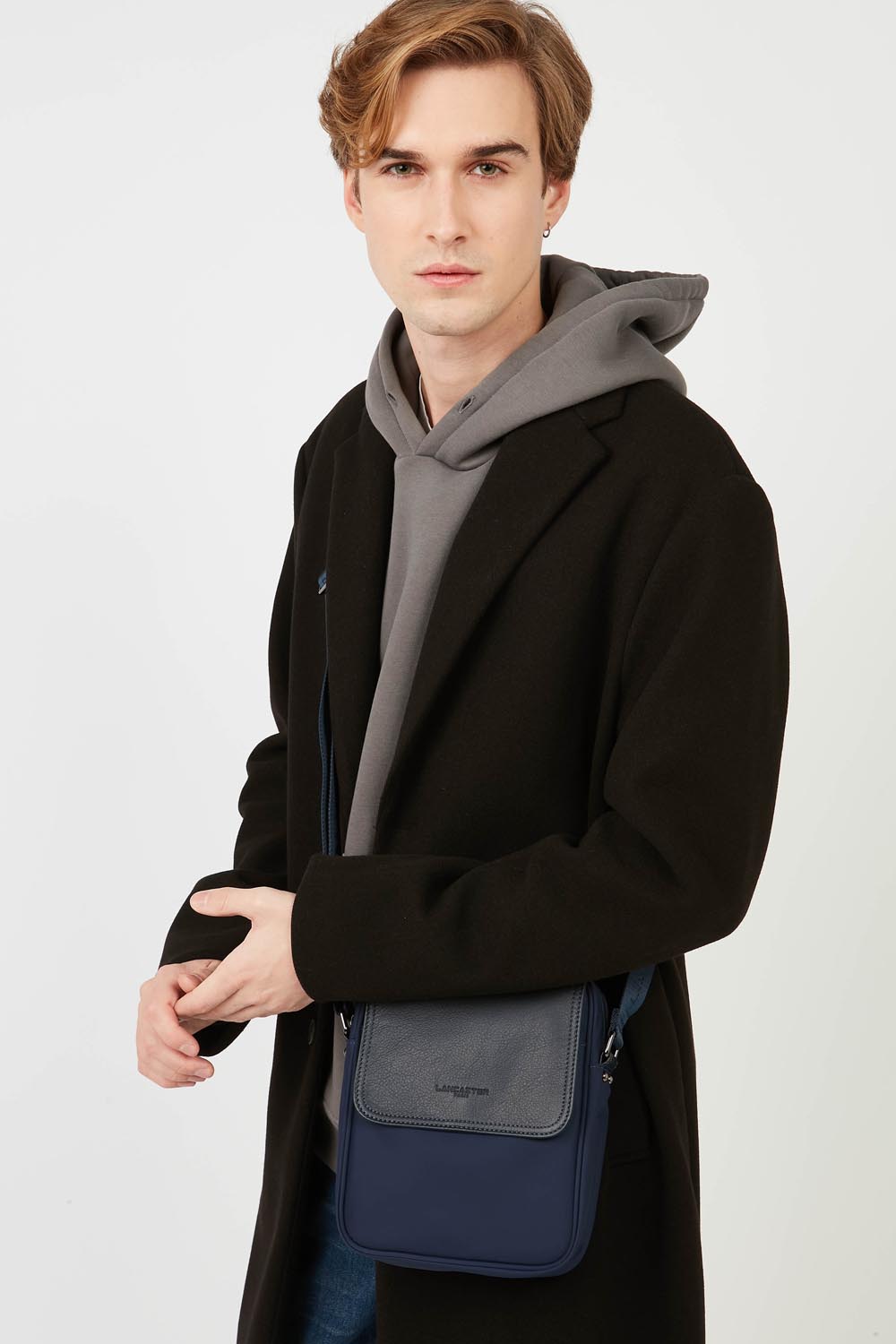 Lancaster Mala Tiracolo Basic Sport Men's Preto – Casaco preto e sweatshirt cinzenta com a mala a tiracolo Basic Sport e calças de ganga azuis.