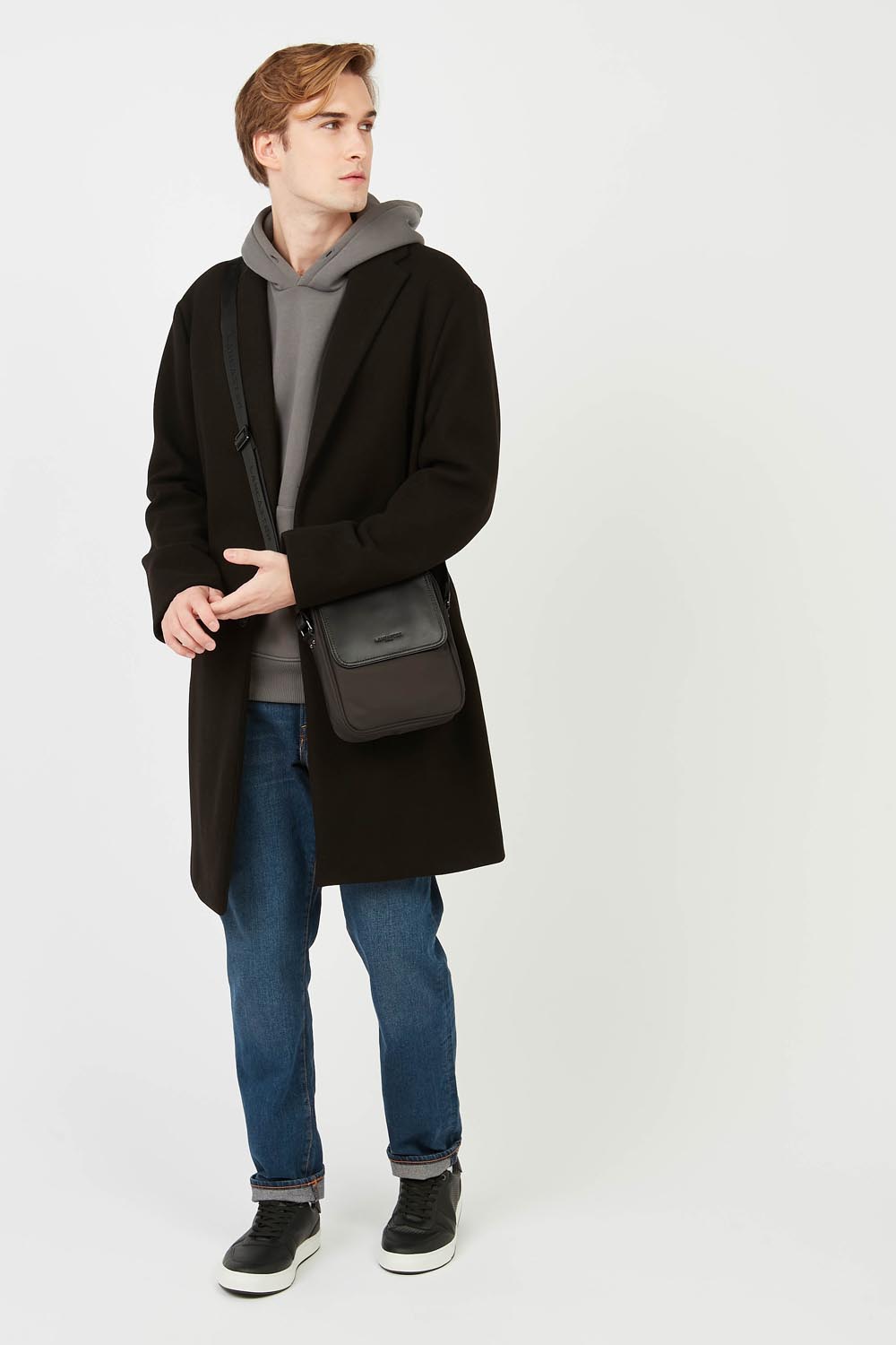 Lancaster Mala Tiracolo Basic Sport Men's Preto – A mala a tiracolo Basic Sport combina com um casaco preto, uma camisola cinzenta e umas calças de ganga azuis.