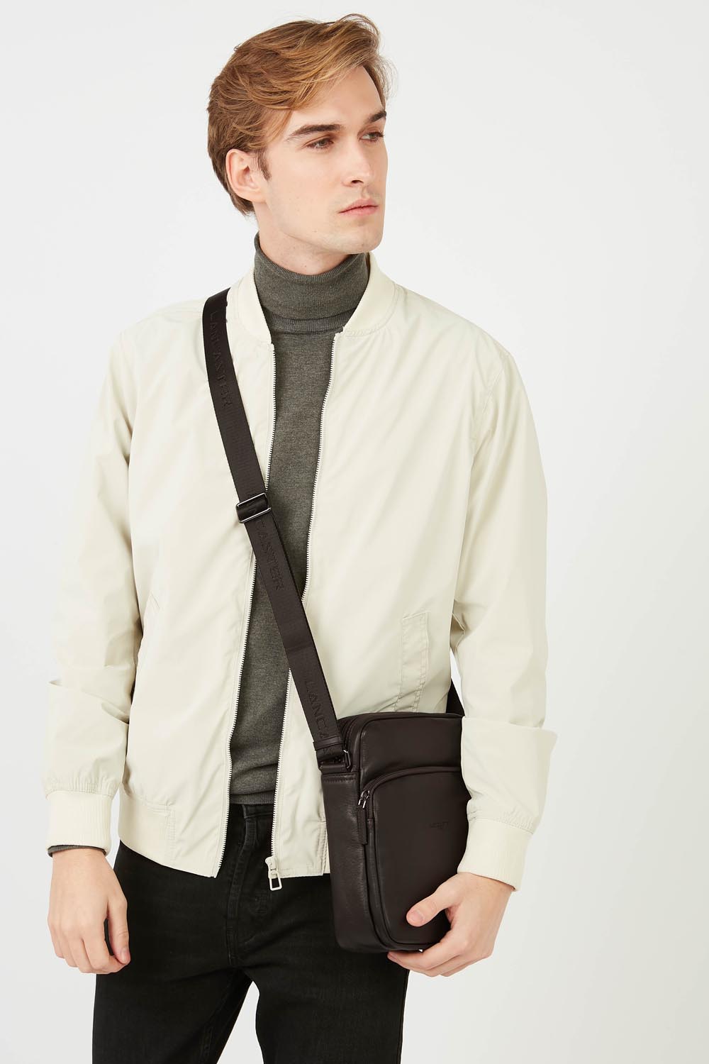 Lancaster besace Soft Vintage marron portée en bandoulière avec une veste écrue, un haut gris et un pantalon noir.