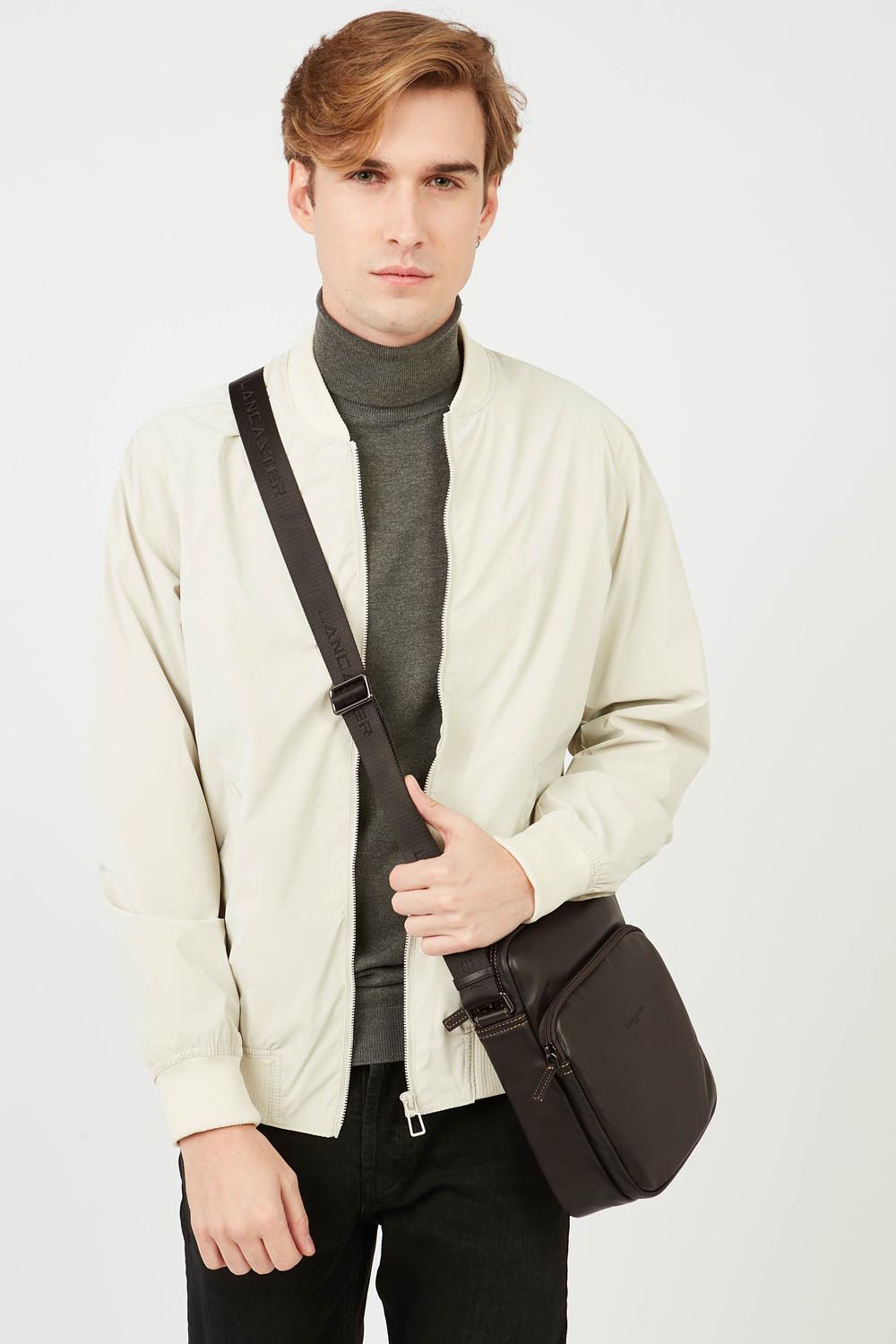 Lancaster besace Soft Vintage noire portée en bandoulière, avec une veste blanche et un haut gris.