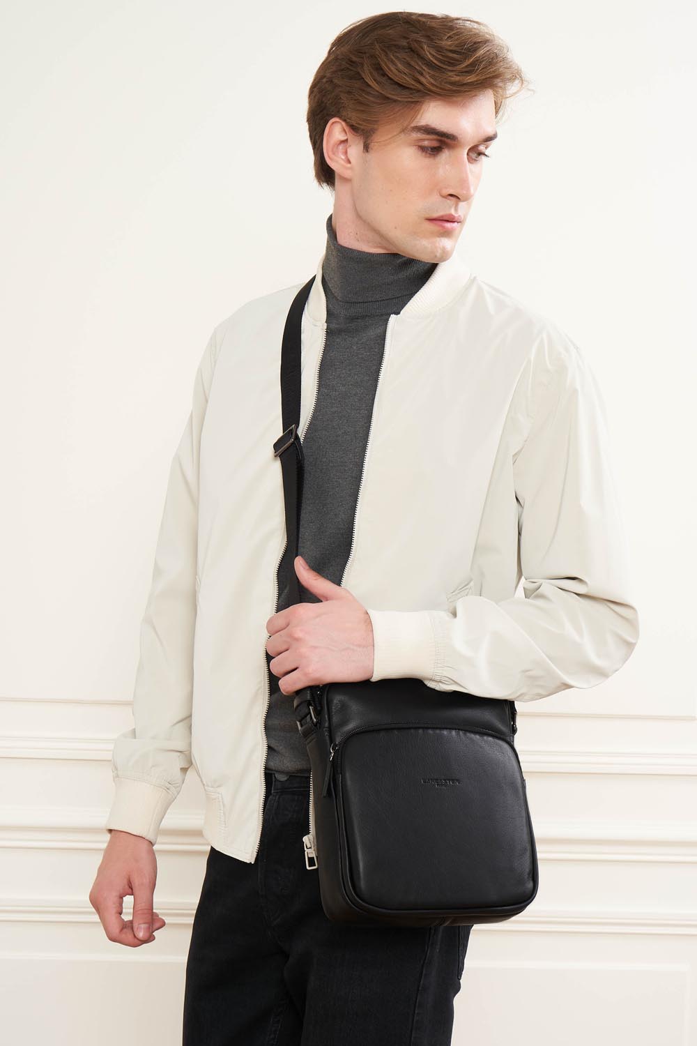 Lancaster besace Soft Vintage noire portée en bandoulière avec une veste claire, un haut gris et un pantalon noir.