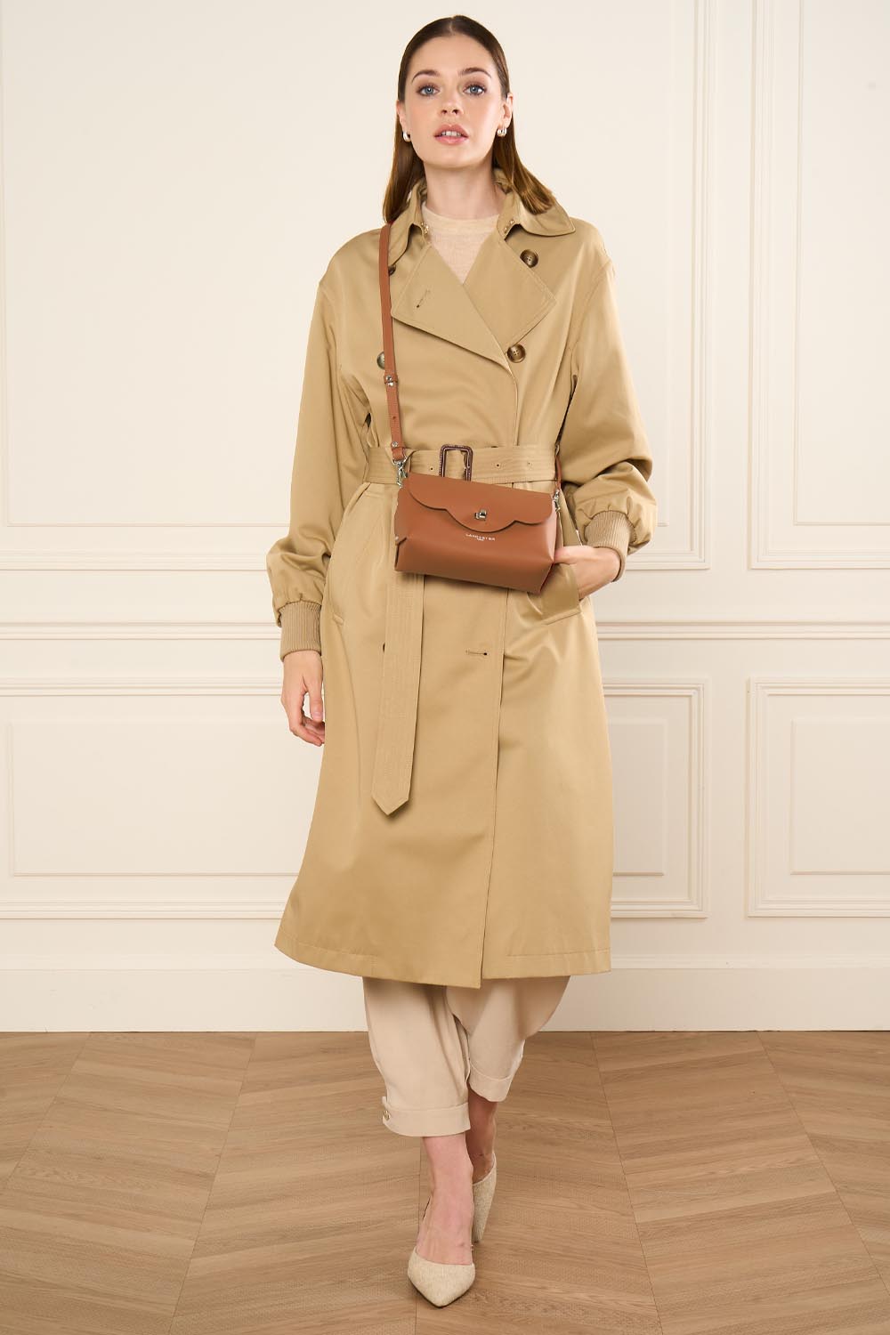 Lancaster Sac rabat PUR & ELEMENT CITY FLORE Noir/Champagne – En bandoulière sur un trench beige, le sac à rabat City Flore s’accorde à un pantalon beige.