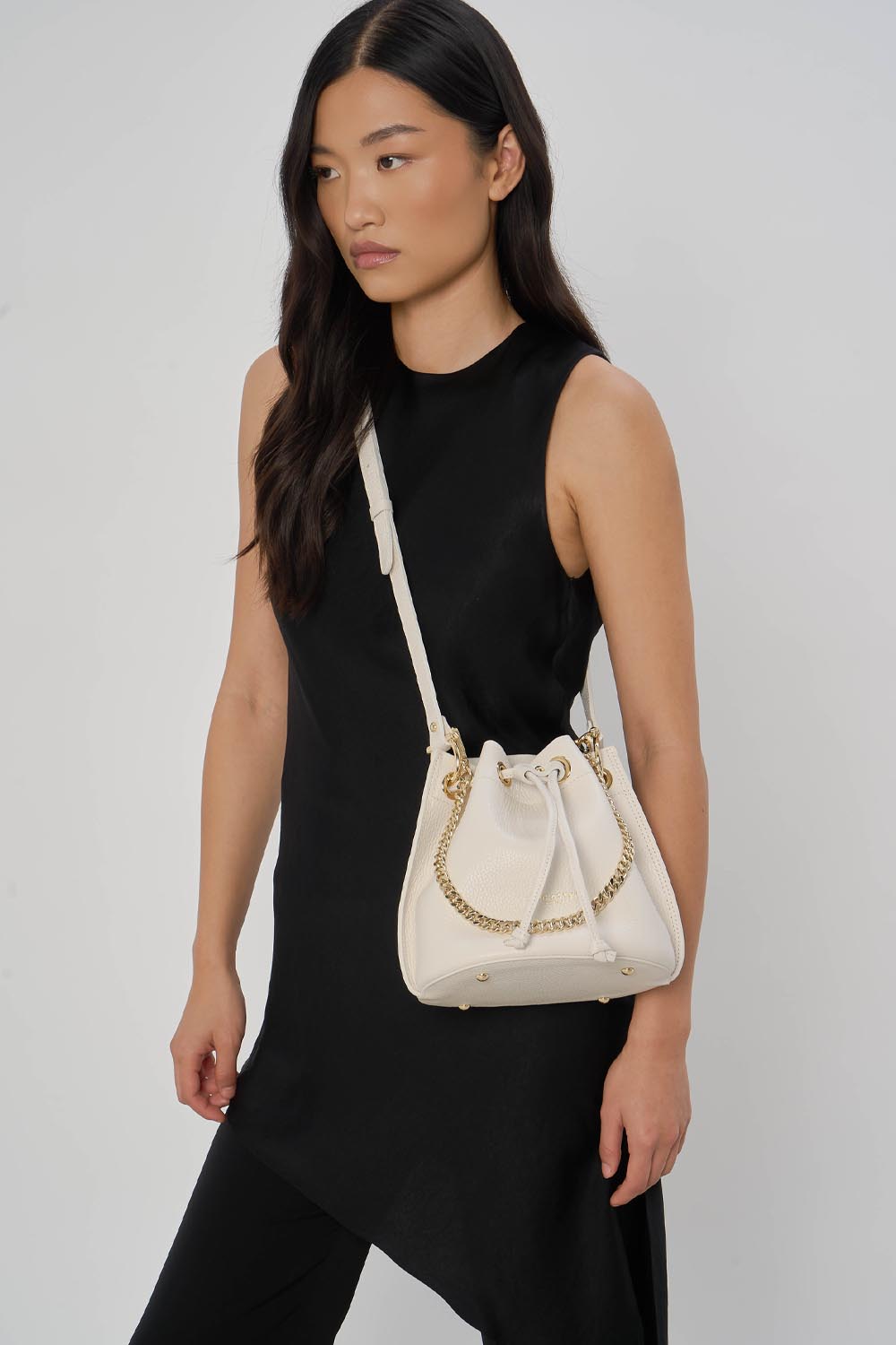 Lancaster Alba Double Bucket Bag Taupe/Gold – The white Alba Double bucket bag is worn crossbody with a sleeveless black dress.