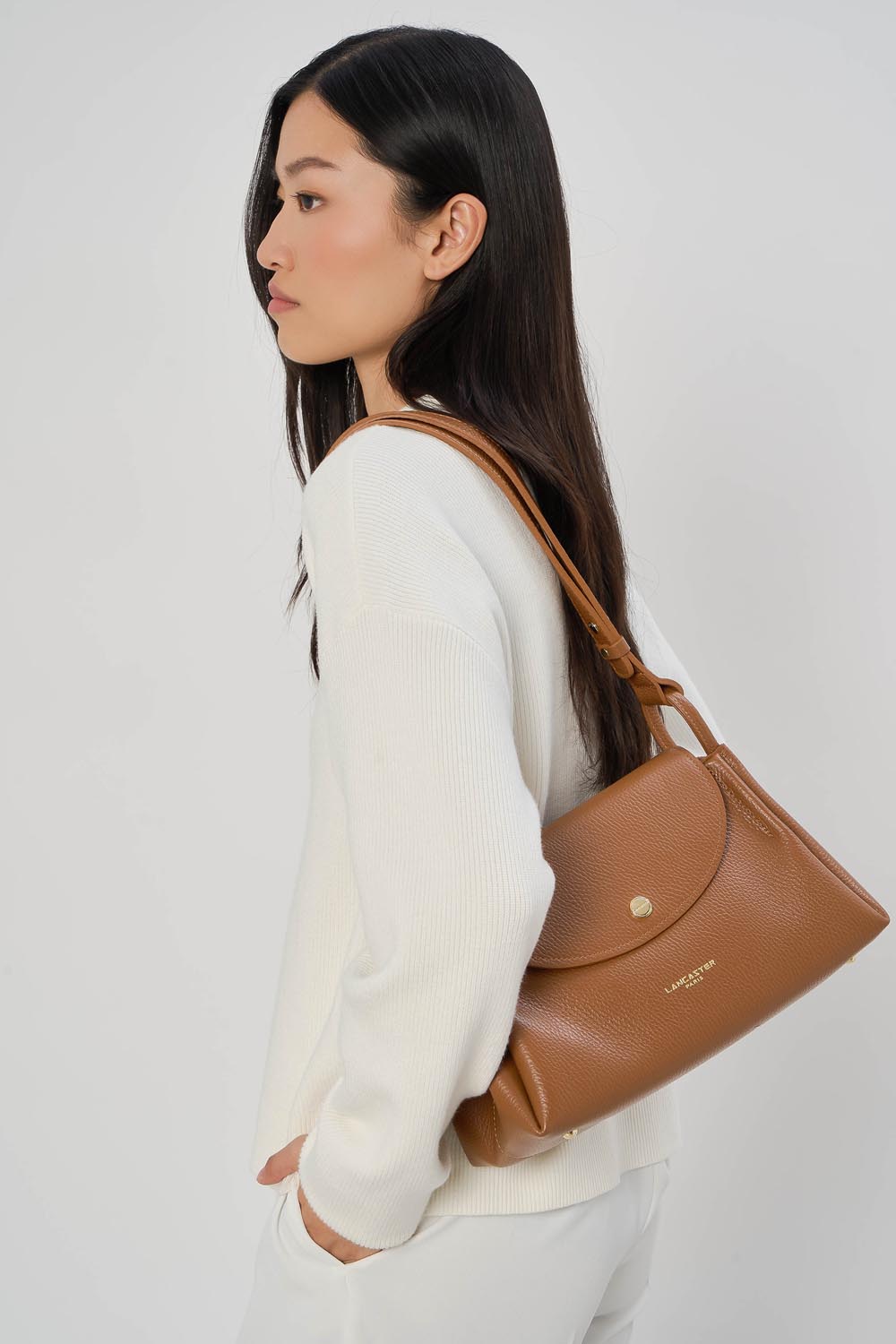 Lancaster Trotteur Bag with Magnetic Flap L Accordéon Double Camel - In - Orange – The Accordéon Double satchel rests on the shoulder with a white sweater and white trousers.