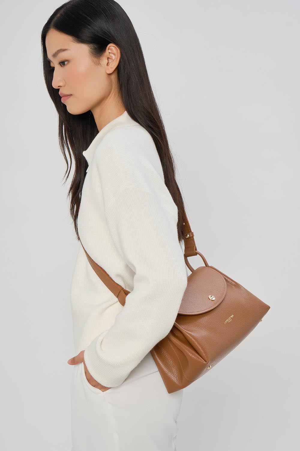 Lancaster Trotteur Bag with Magnetic Flap L Accordéon Double Camel - In - Orange – The brown Trotteur Accordéon Double sits over the shoulder with a white sweater and white trousers.