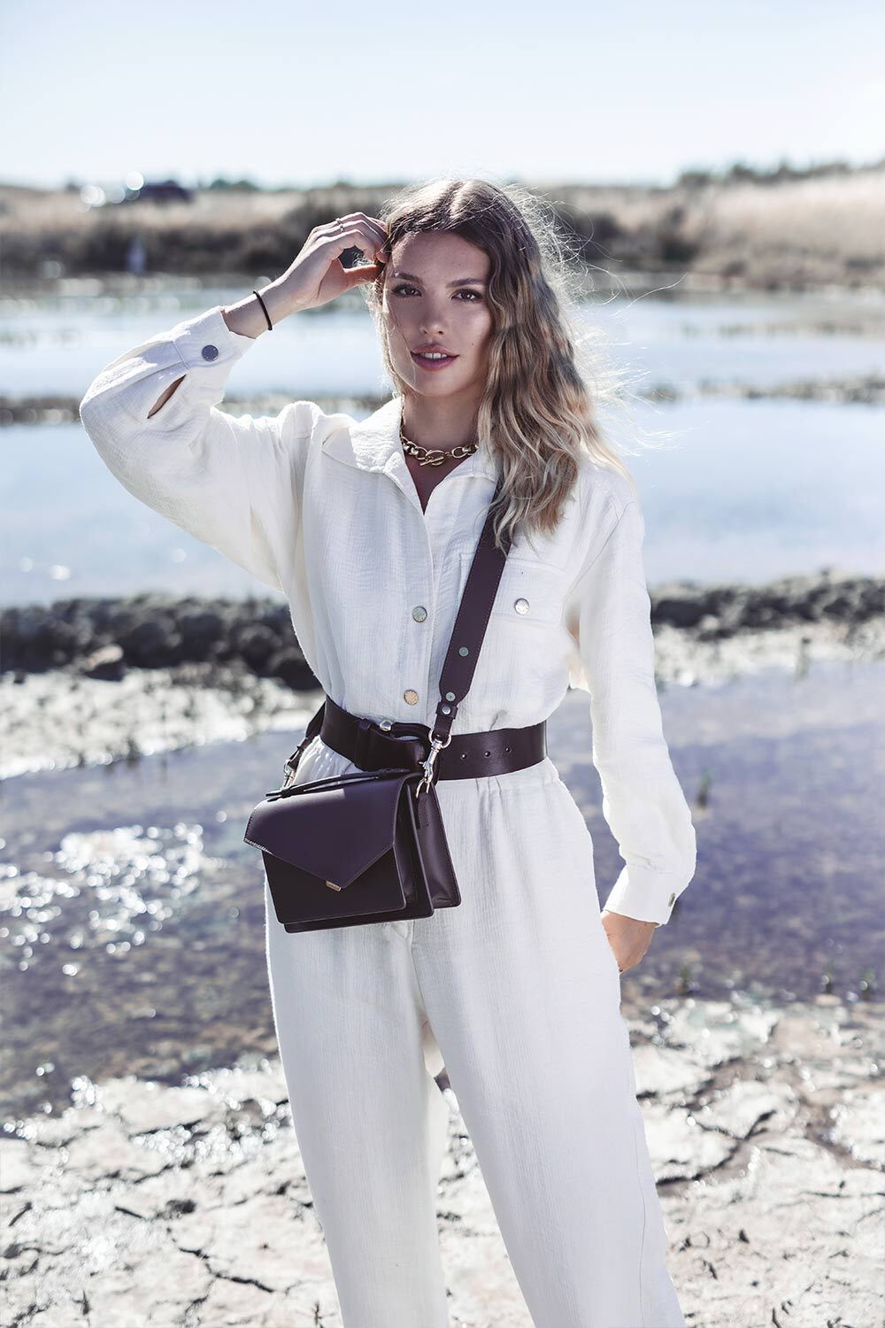 Lancaster Zoé Flap Handbag with Clasp Black – A white jumpsuit and black belt with the Zoé handbag worn crossbody.