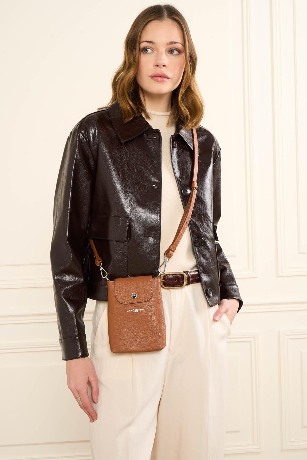 Lancaster Milano Bao Phone Case Dark Blue – The Milano Bao clutch is worn crossbody with a brown jacket and off-white trousers.